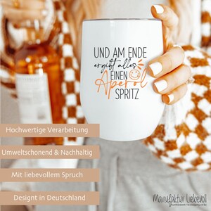 May include: A white insulated wine tumbler with the text "UND AM ENDE ergibt alles EINEN Aperol SPRITZ" in black and orange. The tumbler is held by a person with white nail polish. The image also includes text in German.