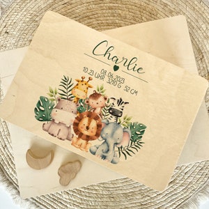 Op de afbeelding: Een houten plaquette met een jungledieren thema, met een giraffe, nijlpaard, aap, zebra, leeuw en olifant. De plaquette is gepersonaliseerd met de naam "Charlie" en de datum "08.06.2023" samen met de tijd "10.23 Uhr", het gewicht "3210 G" en de lengte "52 CM".