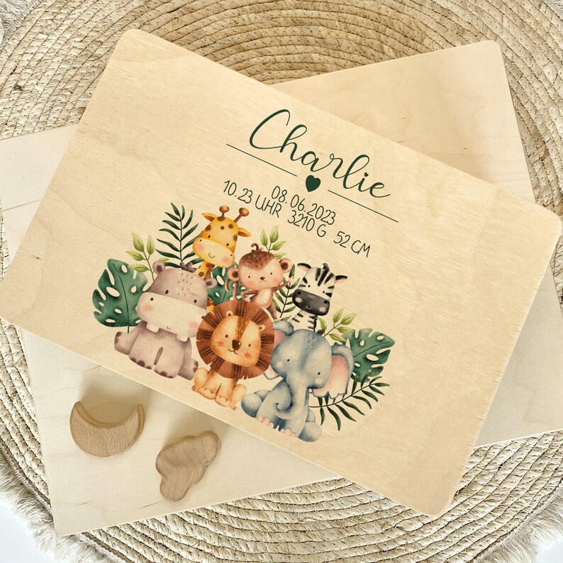 Op de afbeelding: Een houten plaquette met een jungledieren thema, met een giraffe, nijlpaard, aap, zebra, leeuw en olifant. De plaquette is gepersonaliseerd met de naam "Charlie" en de datum "08.06.2023" samen met de tijd "10.23 Uhr", het gewicht "3210 G" en de lengte "52 CM".