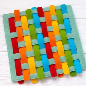 May include: A woven felt mat with colorful strips in red, orange, yellow, green, blue, and turquoise. The strips are woven together in a criss-cross pattern.