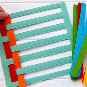 May include: A turquoise felt board with six horizontal slots and a set of colorful felt strips in red, orange, yellow, green, blue, and light blue. The strips are woven through the slots on the board.