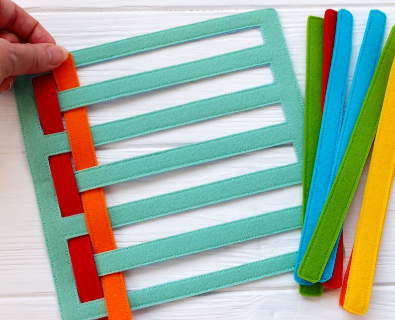 May include: A turquoise felt board with six horizontal slots and a set of colorful felt strips in red, orange, yellow, green, blue, and light blue. The strips are woven through the slots on the board.