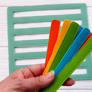 May include: A set of six felt strips in various colors, including green, blue, orange, and yellow. The strips are arranged in a fan shape and held in a hand.