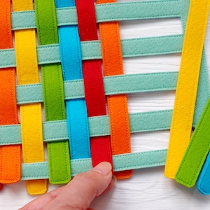 May include: A woven felt mat with strips of red, orange, yellow, green, blue and light blue felt. The mat is woven in a criss-cross pattern.