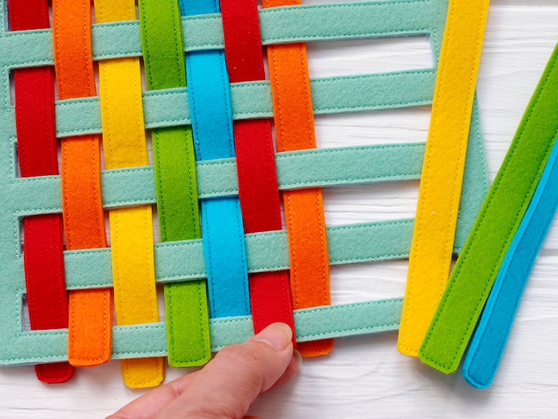 May include: A woven felt mat with strips of red, orange, yellow, green, blue and light blue felt. The mat is woven in a criss-cross pattern.