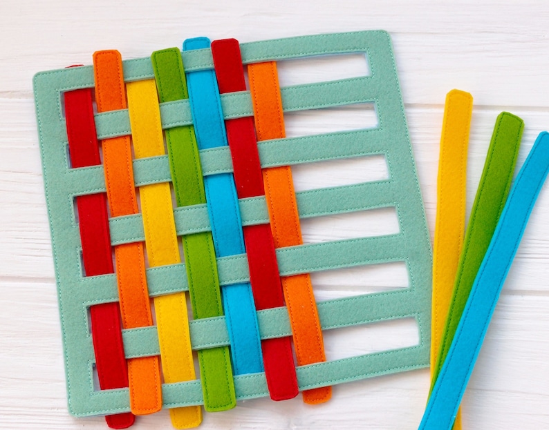 May include: A green felt board with cutouts for weaving colorful felt strips. The strips are red, orange, yellow, green, blue, and purple.