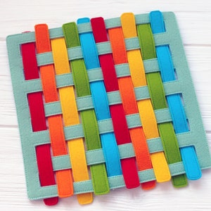 May include: A woven felt mat with colorful strips in red, orange, yellow, green, and blue. The strips are woven together in a criss-cross pattern on a light blue background.