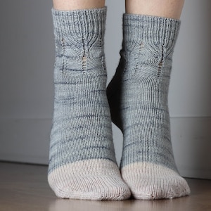 May include: A pair of grey and white knitted socks with a delicate lace pattern around the ankle.