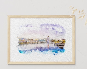 Pode incluir: Uma pintura em aquarela de uma cidade com uma torre alta no centro. A pintura está emoldurada em uma moldura de madeira clara e está pendurada em uma parede branca. Há livros e um relógio em uma mesa de madeira em primeiro plano.
