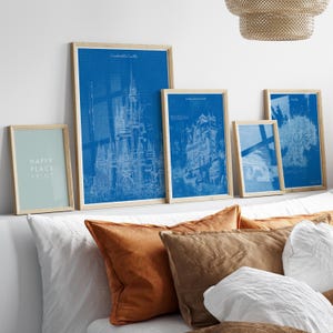Peut inclure: Cinq impressions encadrées de plans architecturaux bleus de châteaux et de bâtiments. Les impressions sont accrochées à un mur blanc au-dessus d'un lit avec des oreillers bruns et blancs. Le texte "Happy Place Print" est sur la plus petite impression.