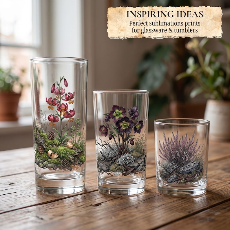 May include: Three clear glass tumblers of varying heights, each featuring a detailed botanical illustration. The designs include red lily-like flowers, dark purple hellebore flowers, and a cluster of purple heather, all set against mossy rocks.