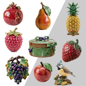 Peut inclure: Une collection d'objets d&eacute;coratifs en c&eacute;ramique comprenant une grenade rouge, une poire jaune, un ananas, une framboise rouge, un panier rond avec des feuilles et des baies vertes, une fraise, des raisins violets, une pomme rouge et un oiseau bleu et jaune.