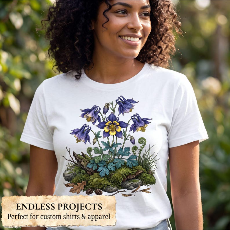 May include: A white t-shirt featuring a detailed graphic illustration of purple and yellow columbine flowers growing from a mossy rock base with green foliage, small pinecones, and fallen oak leaves centered on the front of the garment.