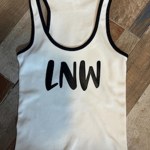 May include: White ribbed tank top with black trim and the letters "LNW" printed in black across the front. The tank top has a racerback design.