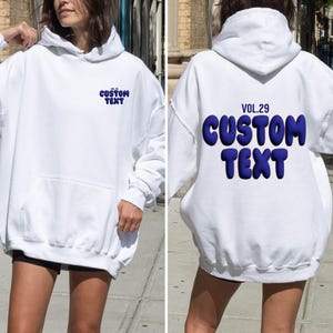 May include: White hoodie with a front pocket and a hood. The front of the hoodie has the text "CUSTOM TEXT" in blue. The back of the hoodie has the text "VOL.29 CUSTOM TEXT" in blue.