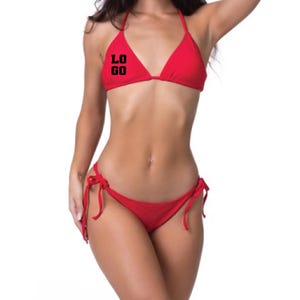 May include: A bright red bikini set featuring a triangle top with thin straps and matching tie-side bottoms. The right side of the triangle top displays the black text "LOGO" printed in a bold, block-style font across the fabric surface.