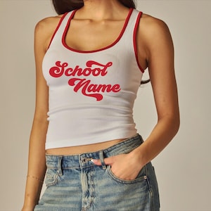 May include: White ribbed tank top with red trim and the words "School Name" in red script. The tank top is a fitted style.