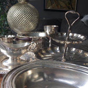 May include: A silver serving tray with a large, round bowl, a smaller bowl, and a two-tiered serving stand with a silver goblet. The tray is decorated with a beaded edge.