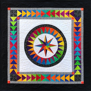 May include: A colorful quilt with a starburst design in the center. The quilt is surrounded by a black border and a white border with a black and white striped pattern. The quilt is made up of various colors, including red, orange, yellow, green, blue, purple, and black.
