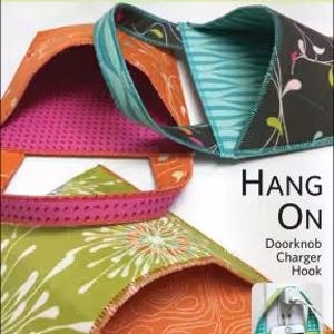 May include: A colorful fabric door knob charger hook with the text "Hang On". The hook is made of various patterned fabrics in orange, green, pink, and teal. The dimensions are 5 inches by 8 inches.