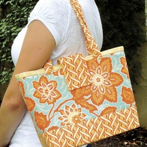 May include: A large tote bag with a floral print in shades of orange, yellow, and blue. The bag has a zippered pocket on the front and a top zipper closure.