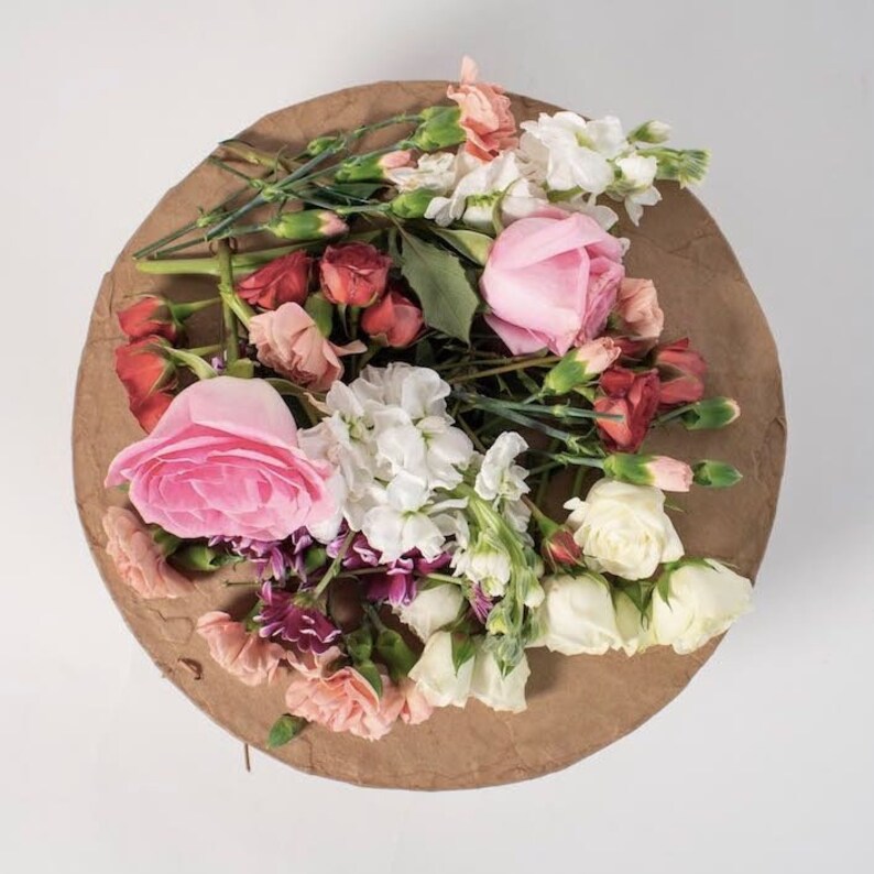 Pu&ograve; includere: Un mazzo di fiori rosa, bianchi e rossi su uno sfondo di carta marrone. I fiori includono rose, garofani e bocche di leone.