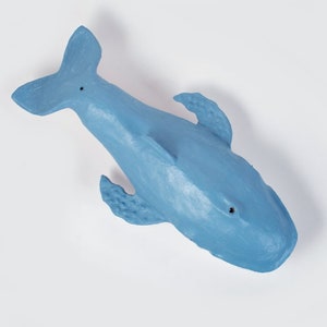 May include: A blue plastic whale toy. The whale is facing upwards with its tail in the air. The whale has a textured surface and a small hole in its eye.