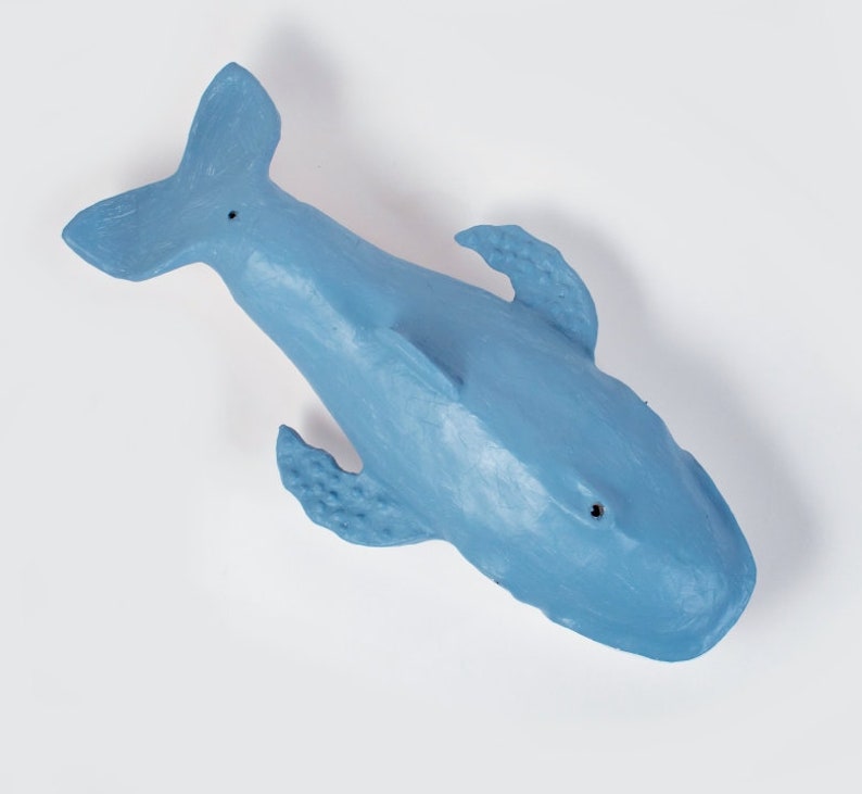 May include: A blue plastic whale toy. The whale is facing upwards with its tail in the air. The whale has a textured surface and a small hole in its eye.