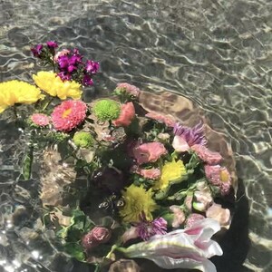 Pu&ograve; includere: Un bouquet di fiori colorati, tra cui giallo, rosa, viola e bianco, immersi in acqua limpida. I fiori sono disposti in cerchio, creando una scena bellissima ed eterea.