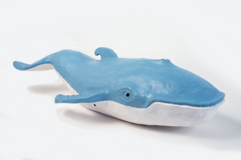 May include: A blue and white whale sculpture made of paper mache. The whale is swimming with its mouth open.