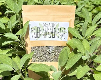 May include: A light brown paper pouch containing dried green herbs, with a white label featuring the text "ORGANIC DRIED GARDEN SAGE" in black lettering. The pouch has a clear window at the bottom revealing the contents of the dried sage leaves.