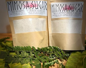 May include: Two brown paper pouches containing Mimosa Sugar, labeled with the text "Mimosa Sugar" and "Tree of Happiness (Albizia Julibrissin)." The Persian Silk Tree is known as the tree of happiness and is credited with a wide range of health benefits.