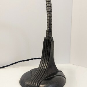 May include: A black metal desk lamp with a flexible gooseneck arm and a decorative base. The lamp has a black cord.