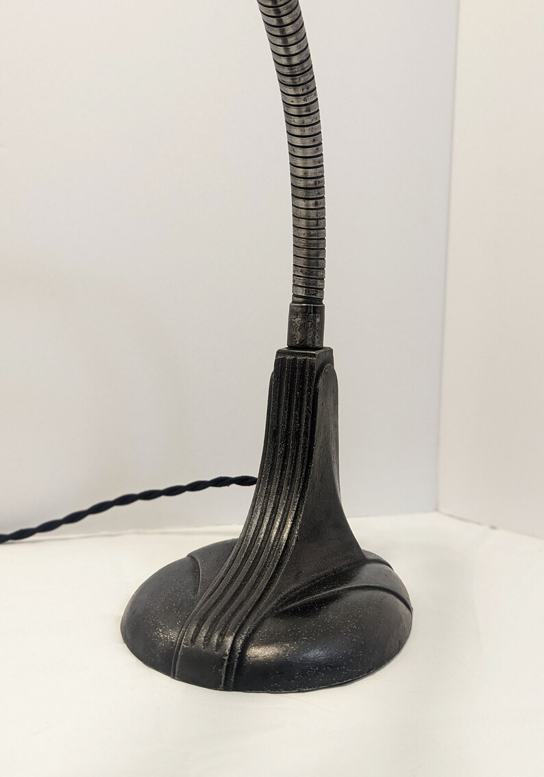 May include: A black metal desk lamp with a flexible gooseneck arm and a decorative base. The lamp has a black cord.