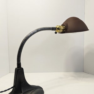May include: A black vintage desk lamp with a flexible gooseneck arm and a brown metal shade. The lamp has a cast iron base.