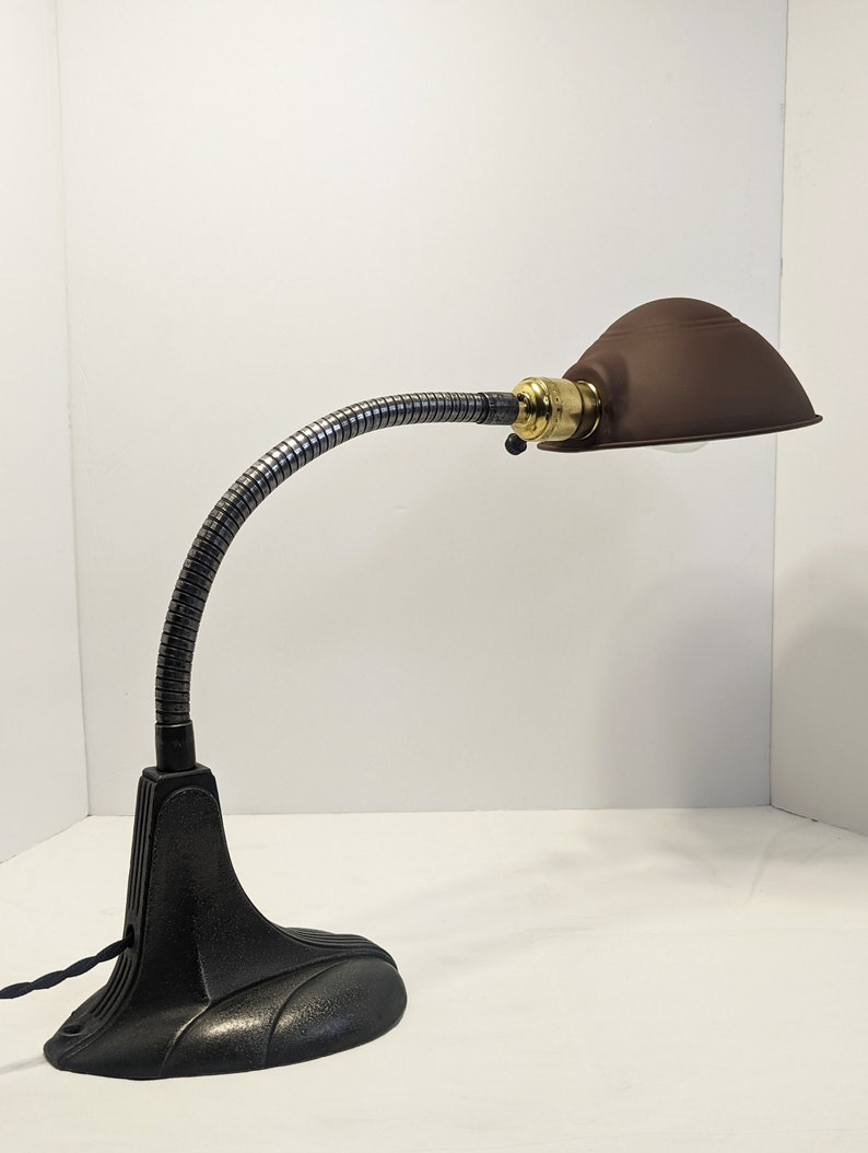 May include: A black vintage desk lamp with a flexible gooseneck arm and a brown metal shade. The lamp has a cast iron base.