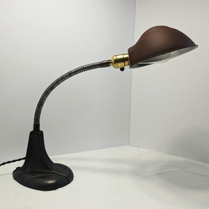 May include: A black and silver adjustable desk lamp with a brown metal shade. The lamp has a flexible arm and a round base.