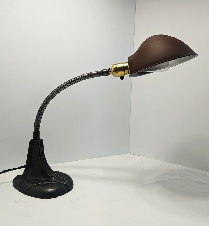 May include: A black and silver adjustable desk lamp with a brown metal shade. The lamp has a flexible arm and a round base.