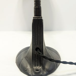 May include: Black metal desk lamp with a flexible arm and a round base. The lamp has a cord with a black braided wire.