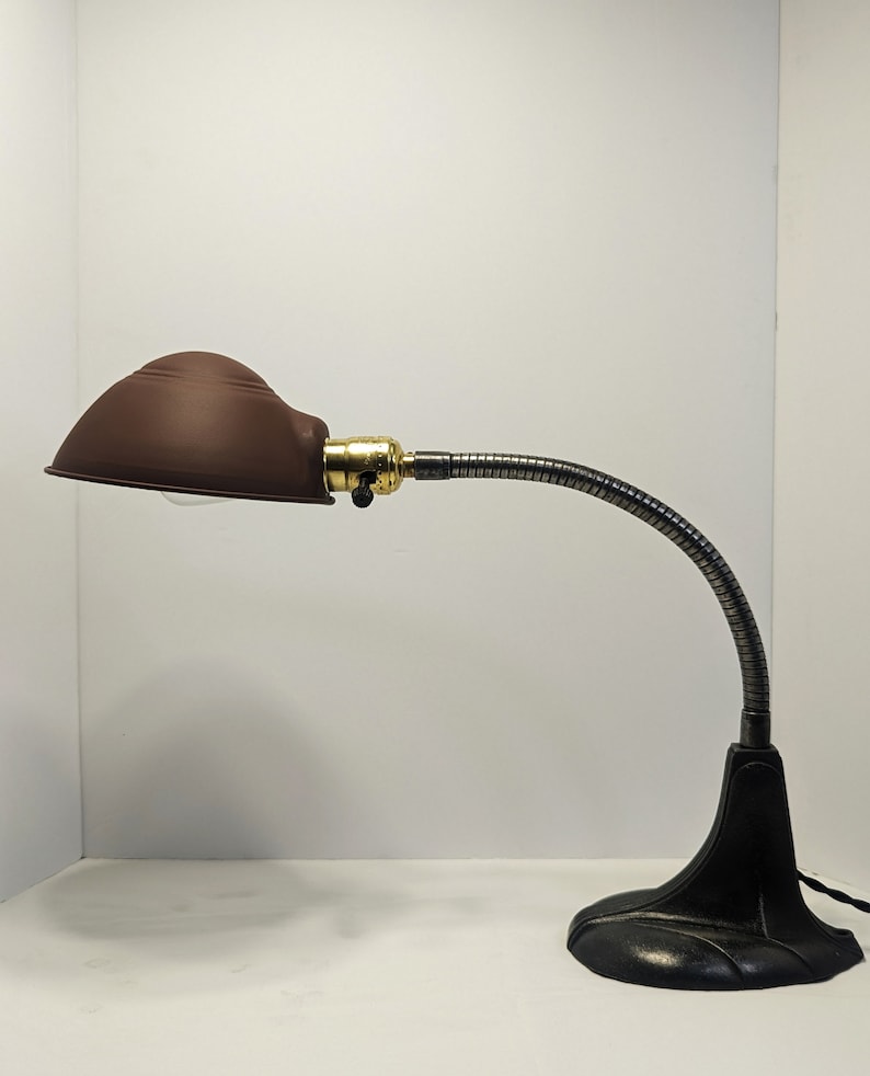 May include: A brown metal desk lamp with a flexible gooseneck arm and a black base. The lamp has a brown metal shade.