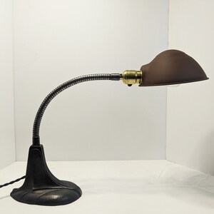 May include: A black metal desk lamp with a flexible gooseneck arm and a brown metal shade. The lamp has a classic design and is in good condition.