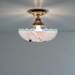 May include: A vintage ceiling light fitting with a brass finish and a frosted glass bowl-shaped shade. The shade has a scalloped edge and a delicate floral pattern. A small chain hangs from the fitting.