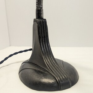 May include: A black metal desk lamp with a flexible arm and a decorative base. The base has a smooth, rounded shape with a textured surface.