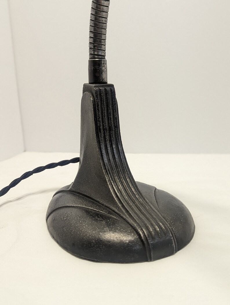 May include: A black metal desk lamp with a flexible arm and a decorative base. The base has a smooth, rounded shape with a textured surface.