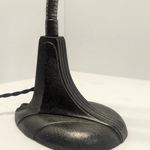 May include: A black metal desk lamp with a flexible arm and a weighted base. The base has a decorative design with curved lines.