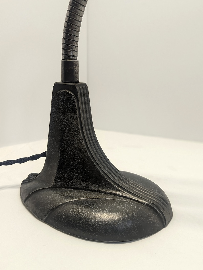 May include: A black metal desk lamp with a flexible arm and a weighted base. The base has a decorative design with curved lines.