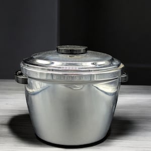 May include: A silver ice bucket with a black lid and handles. The bucket is made of metal and has a shiny finish.