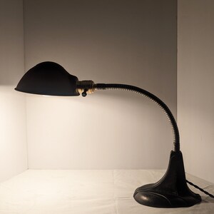 May include: A black metal desk lamp with a flexible arm and a dome-shaped shade. The lamp is on a white surface.