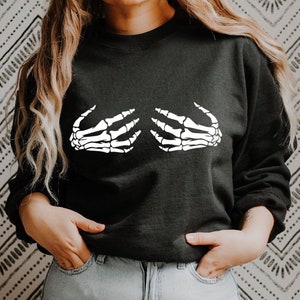 May include: Black sweatshirt with a white skeleton hand graphic on the front. The hands are positioned as if they are covering the chest.
