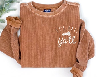 May include: A brown waffle knit long-sleeve shirt with the text "It's Fall Ya'll" in white lettering. The shirt features a small graphic of a truck with pumpkins on the back.